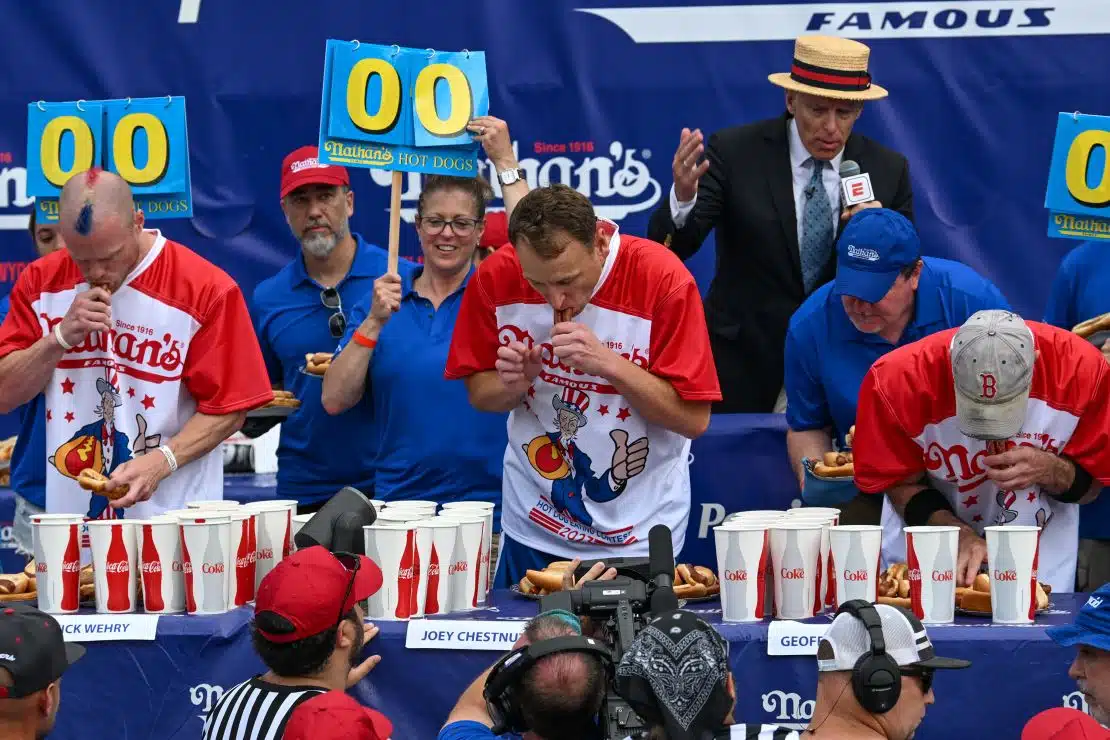 NEW YORK, NEW YORK - JULY 04: Defending champion Joey Chestnut (C) competes in the 2023 Nathan's Famous Fourth of July International Hot Dog Eating Contest on July 4, 2023 at Coney Island in the Brooklyn borough of New York City. The men's contest was postponed due to thunderstorms but later happened without spectators allowed into the